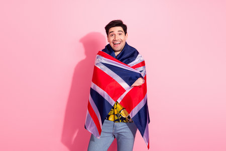Young man with a Union Jack flag smiling against a pink background demonstrating vibrant energy and patriotismの写真素材
