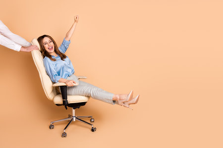 Confident businesswoman enjoying a fun moment in an office chair against a beige background, showcasing happiness and styleの写真素材
