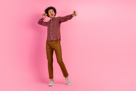 Energetic young man with vibrant style posing dynamically against a bright pink background, expressing joy and enthusiasmの写真素材