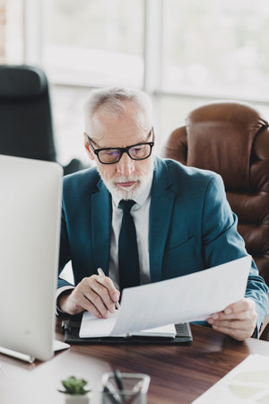 Successful Mature businessman reviewing documents at a desk in an office environmentの写真素材