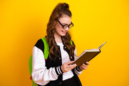 Charming female student wearing stylish sportswear and reading a book against a bright yellow backgroundの写真素材