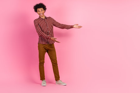 Young man in stylish casual attire presenting gesture on vibrant pink background conveying happiness and enthusiasmの写真素材