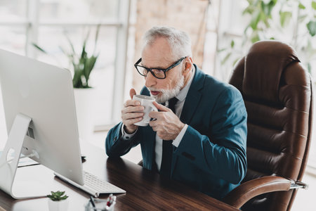 Businessman in formalwear working at his office desk while enjoying a hot beverage for a productive start to the dayの写真素材