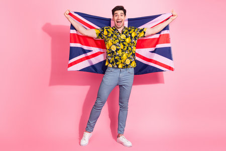 Excited man holding a Union Jack flag on a vibrant pink background wearing a tropical shirt and jeansの写真素材