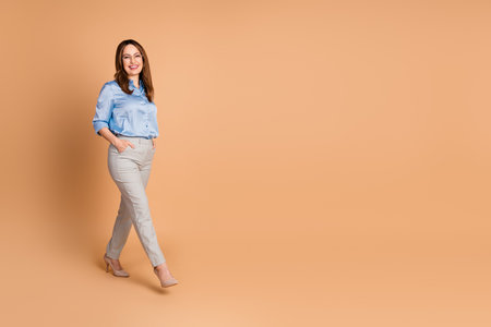 Successful businesswoman walking confidently in an elegant blouse on beige background, showcasing style and successの写真素材