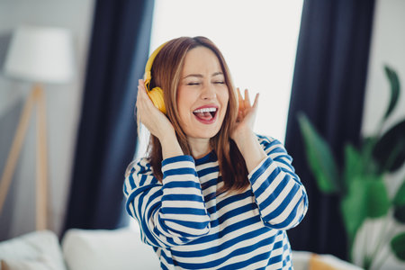 Young woman enjoying music with headphones, cheerful and full of joy in a cozy indoor settingの写真素材