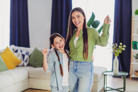Mother and daughter happily holding keys, celebrating a new beginning in a modern living room settingの写真素材