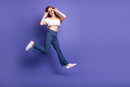 Cheerful young woman jumping in stylish casual clothes with a smile on vibrant purple background