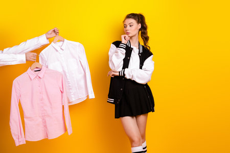 Young female student evaluating style choices with stylish casual jacket outfit on vibrant yellow backgroundの写真素材