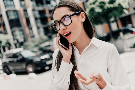 Confident businesswoman talking on phone outdoors against urban background emphasizing professional communicationの写真素材