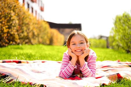 Adorable young girl smiling outdoors in vibrant green grass and springtime sunlight, wearing a striped casual outfitの写真素材