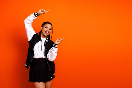 Young girl in casual school outfit gestures joyfully against vibrant orange background, expressing energy and enthusiasmの写真素材