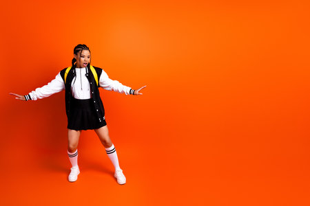 Confident teenage student showing expressive gesture against vibrant orange background in casual sportswearの写真素材