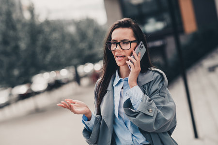Confident young woman talking on phone outdoors in urban setting on a bright day wearing stylish and trendy coatの写真素材