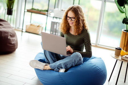 Young Woman Working From Home Seated Comfortably With Laptop in a Stylish Indoor Settingの写真素材
