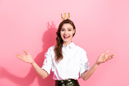 Smiling young woman in a white shirt gesturing joyfully against a vibrant pink backgroundの写真素材