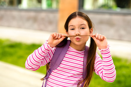 Playful young girl with a striped shirt smiling outdoors against a sunny urban backdrop, showcasing...