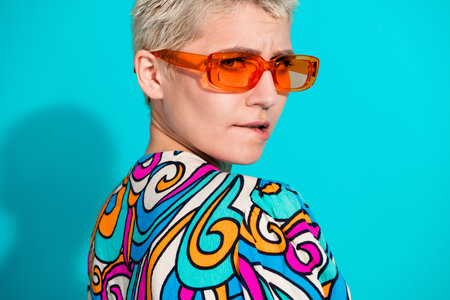 Stylish young woman with vibrant fashion and orange sunglasses against a teal background, showcasing...
