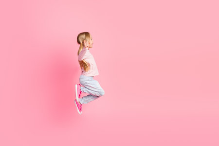 Cute little girl in casual clothes happily jumping on a vibrant pink background with a cheerful...