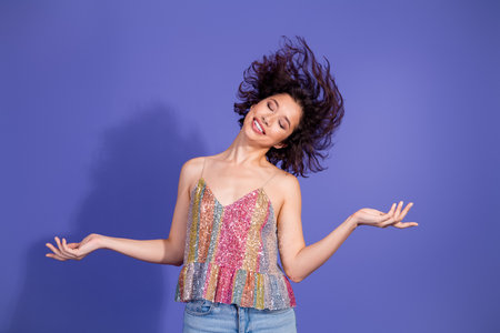 Young fashionable woman in a shiny sequin top posing confidently against a vivid purple background