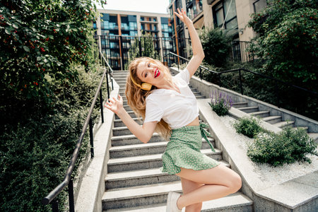 Young woman cheerfully dancing on outdoor stairs in urban setting, embracing summer vibes and...