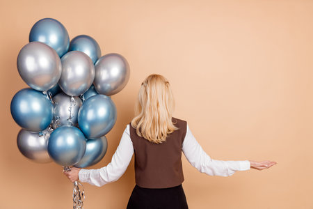 Successful businesswoman standing with balloons against beige background showcasing charm and...