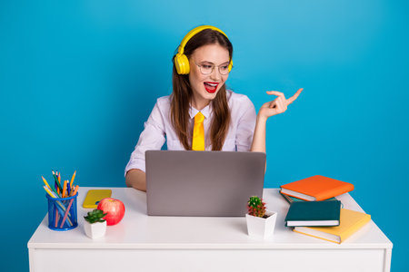 Smiling girl in headphones working on a laptop and enjoying music at her study desk with book and...
