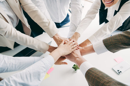 Group of business professionals joining hands in unity at an office to showcase teamwork,...
