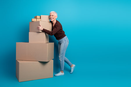 Mature Woman Embracing Stacked Cardboard Boxes Against Vibrant Blue Walls in an Expression of Joy...