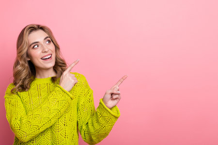 Cheerful young woman in a bright yellow sweater pointing to a pink background, expressing happiness and positive energyの写真素材
