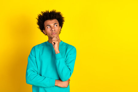 Thoughtful young man in a teal sweatshirt against vibrant yellow background embodying casual style...