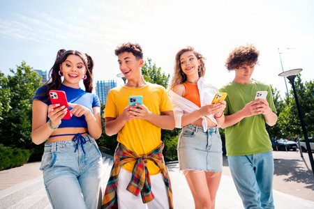 Group of young friends bonding outdoors with smartphones in a sunny cityscape
