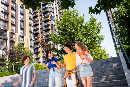 Four friends outdoors enjoying a sunny day in a city setting with greenery and modern architecture