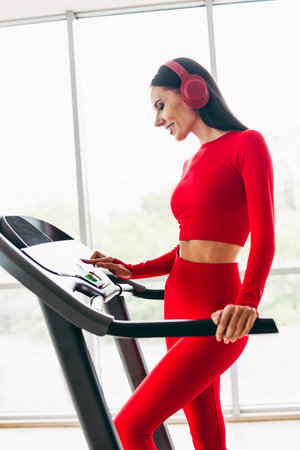Active young woman in vibrant red activewear exercising on a treadmill indoors, enjoying fitness and...