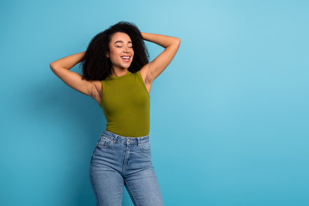 Stylish young woman with curly black hair in casual attire on a blue background exuding confidence...