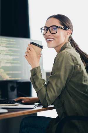 Charming female programmer working at her desk with a cup of coffee in hand in a modern workspace