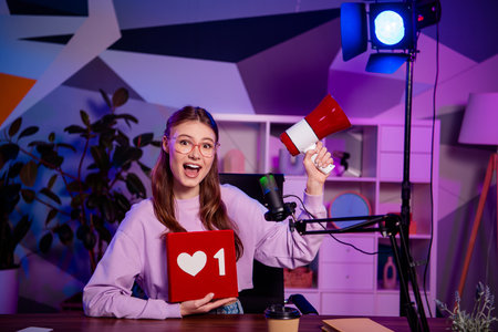Popular female blogger with megaphone hosting a podcast in a vibrant studio, showcasing social media engagement and interactionの写真素材