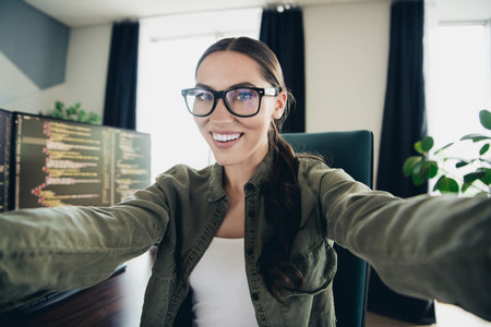 Professional computer programmer smiles confidently at her workspace with monitors displaying code representing remote work and technologyの写真素材