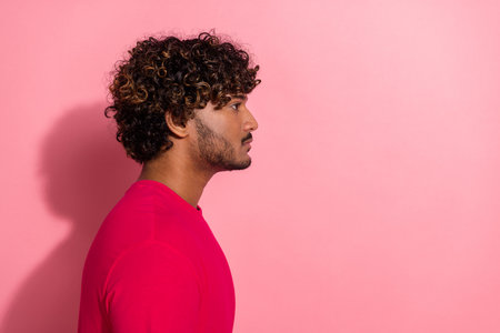 Side profile portrait of a stylish young man with curly hair wearing a red t-shirt against a pink backgroundの写真素材