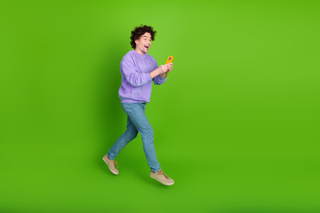 Energetic young male holding a phone with excitement, wearing a purple sweatshirt, standing against a bright green backgroundの写真素材