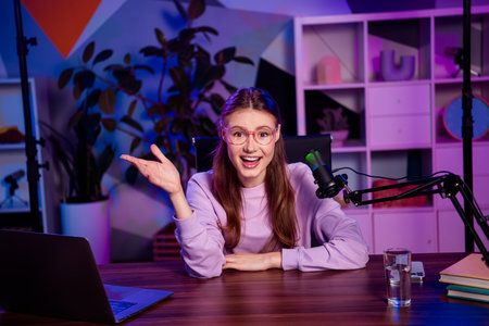 Popular female blogger recording podcast with professional microphone in stylish office setup featuring colorful lightingの写真素材
