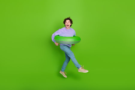 Energetic young man with inflatable ring jumping on green background depicting active lifestyle and joyの写真素材