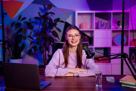 Popular professional female vlogger recording a podcast in a colorful indoor space with neon...