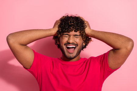 Cheerful young man in a red t-shirt with curly hair on a vibrant pink background expressing...