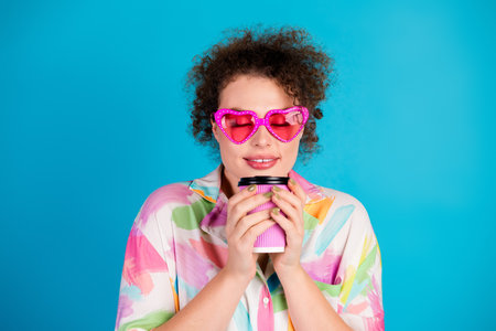 Young female with pink heart-shaped glasses holding a coffee cup, wearing a colorful shirt, on a...