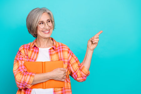 Happy senior woman in a colorful checkered shirt smiling and holding an orange tablet on a teal...