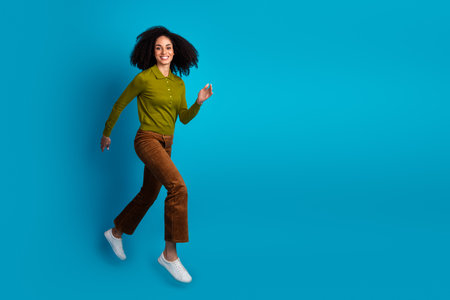 Stylish young woman with afro hairstyle walking confidently against a vibrant blue background...