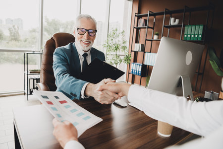 Senior businessman shaking hands with a colleague in his office, symbolizing teamwork and mutual...