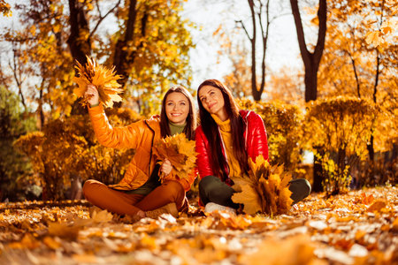 Two young women enjoying a colorful autumn day in a park surrounded by vibrant foliage and sunlight