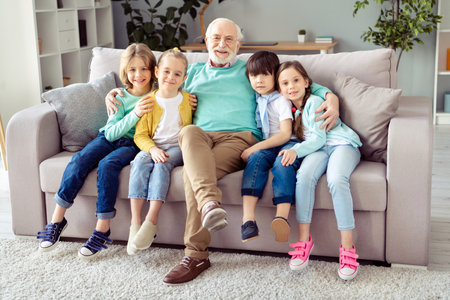 Photo of big happy smiling cheerful family grandfather in glasses hug embrace his grandchildren sit...